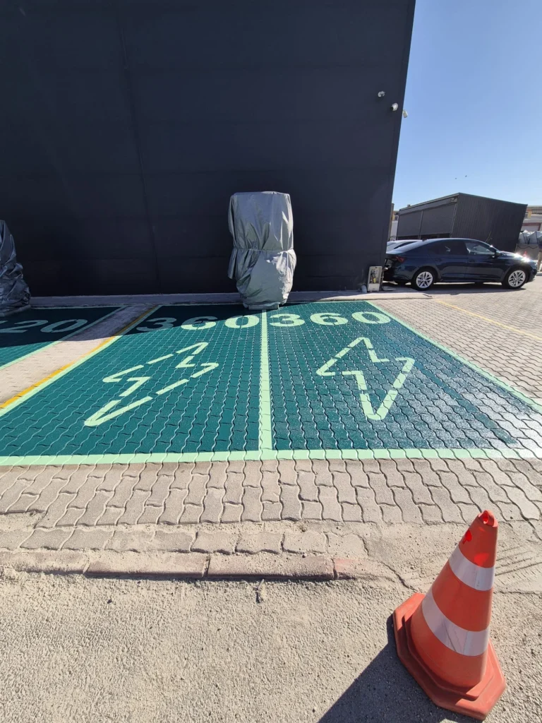 Yeşil zeminli elektrikli araç park yerlerinde şarj sembolleri ve ayırıcı çizgiler