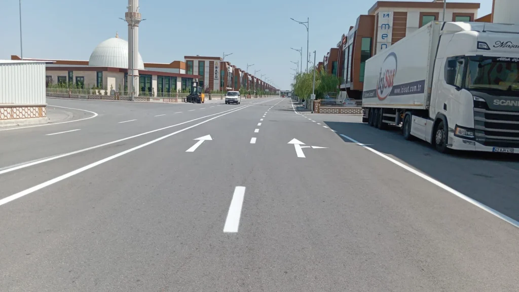 Sanayi sitesi asfalt yolunda beyaz şerit çizgileri ve yönlendirme okları