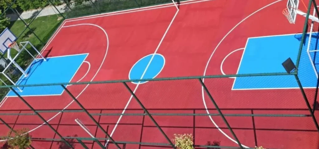 Açık spor sahasında kırmızı ve mavi zemin üzerine uygulanan basketbol, voleybol ve futbol oyun çizgileri