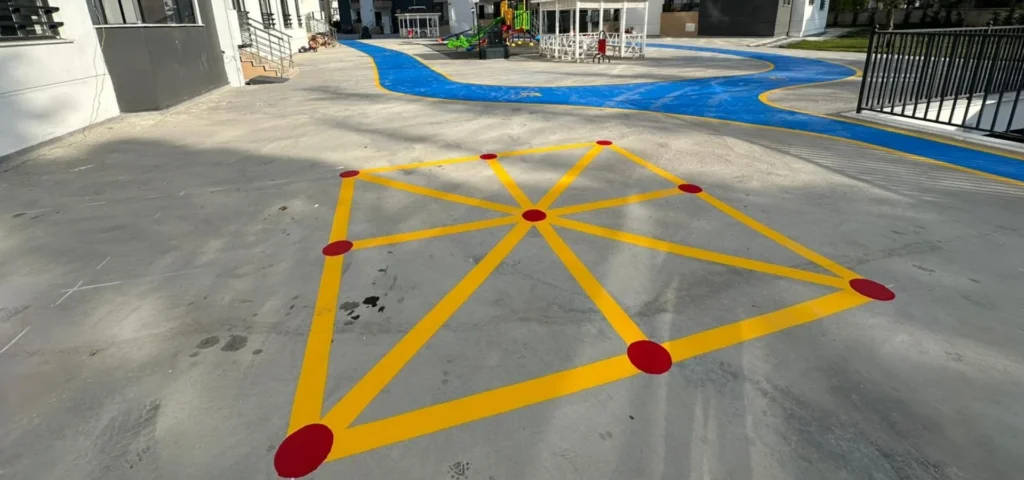 Site bahçesindeki beton zemine uygulanan sarı çizgili ve kırmızı noktalı seksek oyunu
