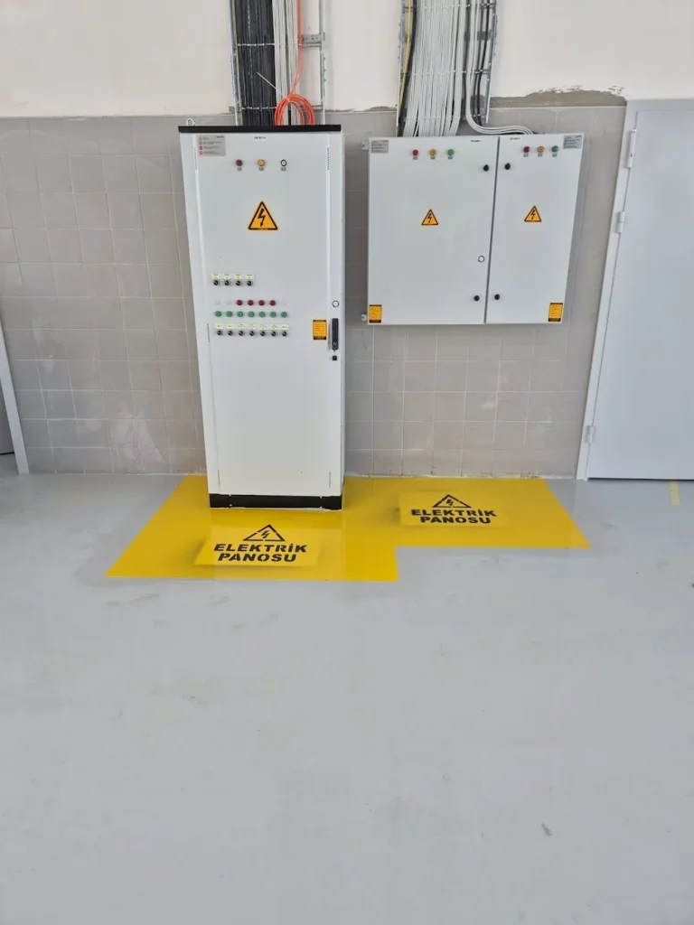 Elektrik panolarının önünde sarı boya ve uyarı yazılarıyla belirlenen güvenlik alanı