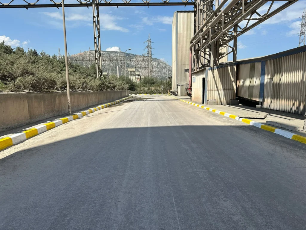Fabrika iç yolundaki kaldırım taşlarına uygulanan sarı-beyaz bordür tarama