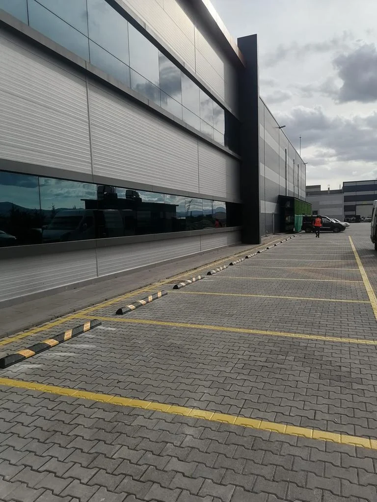 Fabrika otoparkında kilitli taş zemin üzerine uygulanan sarı park yeri çizgileri ve stoperler