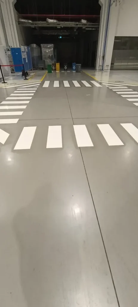 Fabrika içerisindeki gri epoksi zemin üzerine uygulanan beyaz geçiş şeritleri