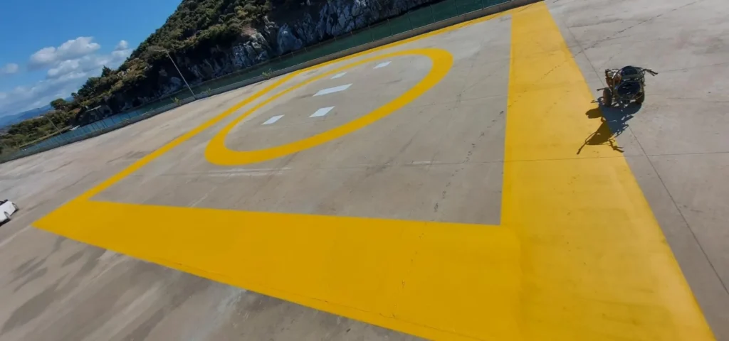 Beton zemine uygulanan sarı helikopter pisti sınır çizgileri ve dairesel iniş alanı işaretlemesi