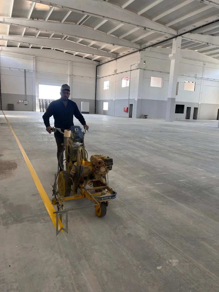 Fabrika beton zeminine makineyle sarı İSG çizgisi uygulayan personel