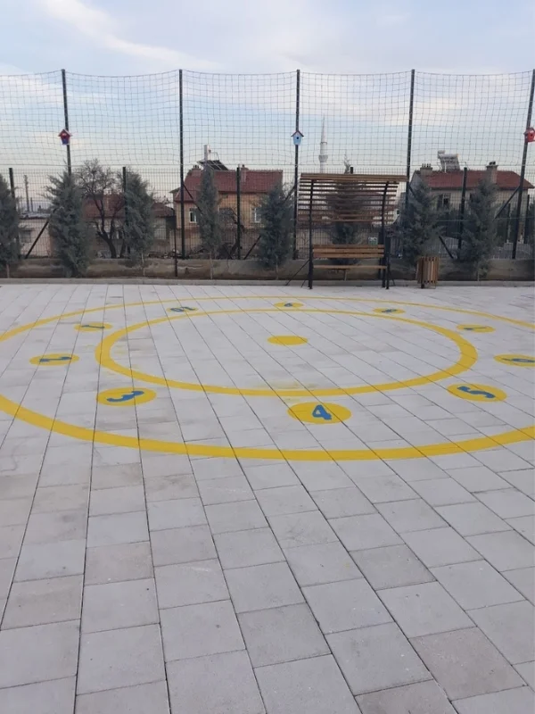 Okul bahçesi taş zeminine sarı çemberler ve rakamlarla uygulanan grup oyunu