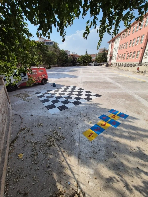 Okul bahçesindeki beton zemine uygulanan siyah-beyaz satranç alanı ve renkli seksek oyunu