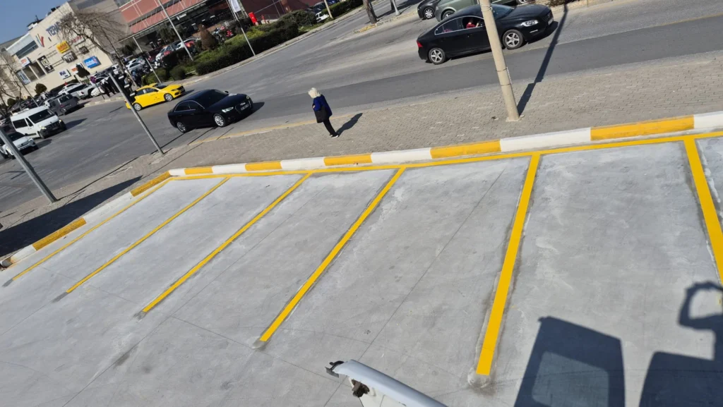 Açık otoparkta sarı park yeri çizgileri ve sarı-beyaz bordür tarama